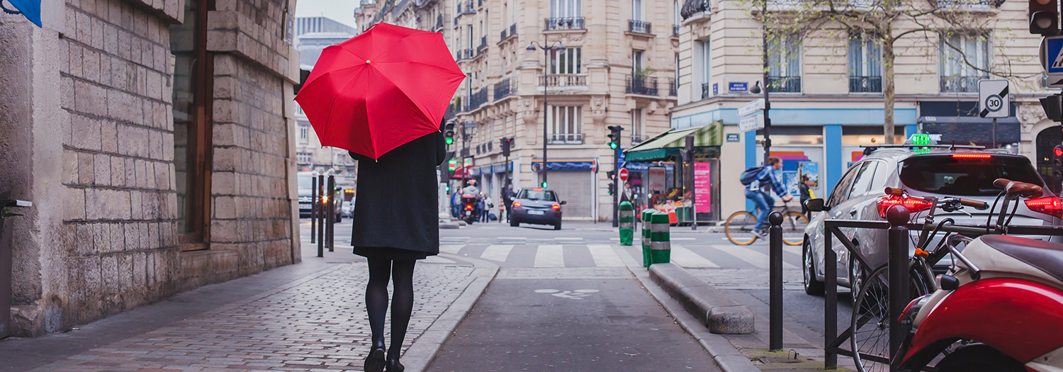 Ambasiøs dame med rød paraply gåt nedover fortauet i en by. Tenker på hvorfor hun skal velge Xledger.