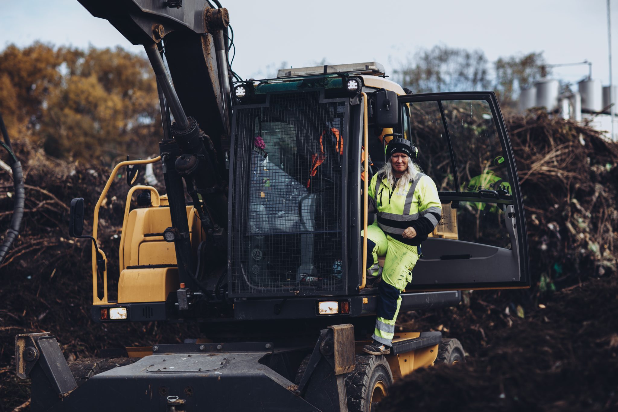 Bilde av en kvinnelig Iris Salten arbeider som er på vei ut av en orange gravemaskin iført signalgult arbeidstøy. Foto