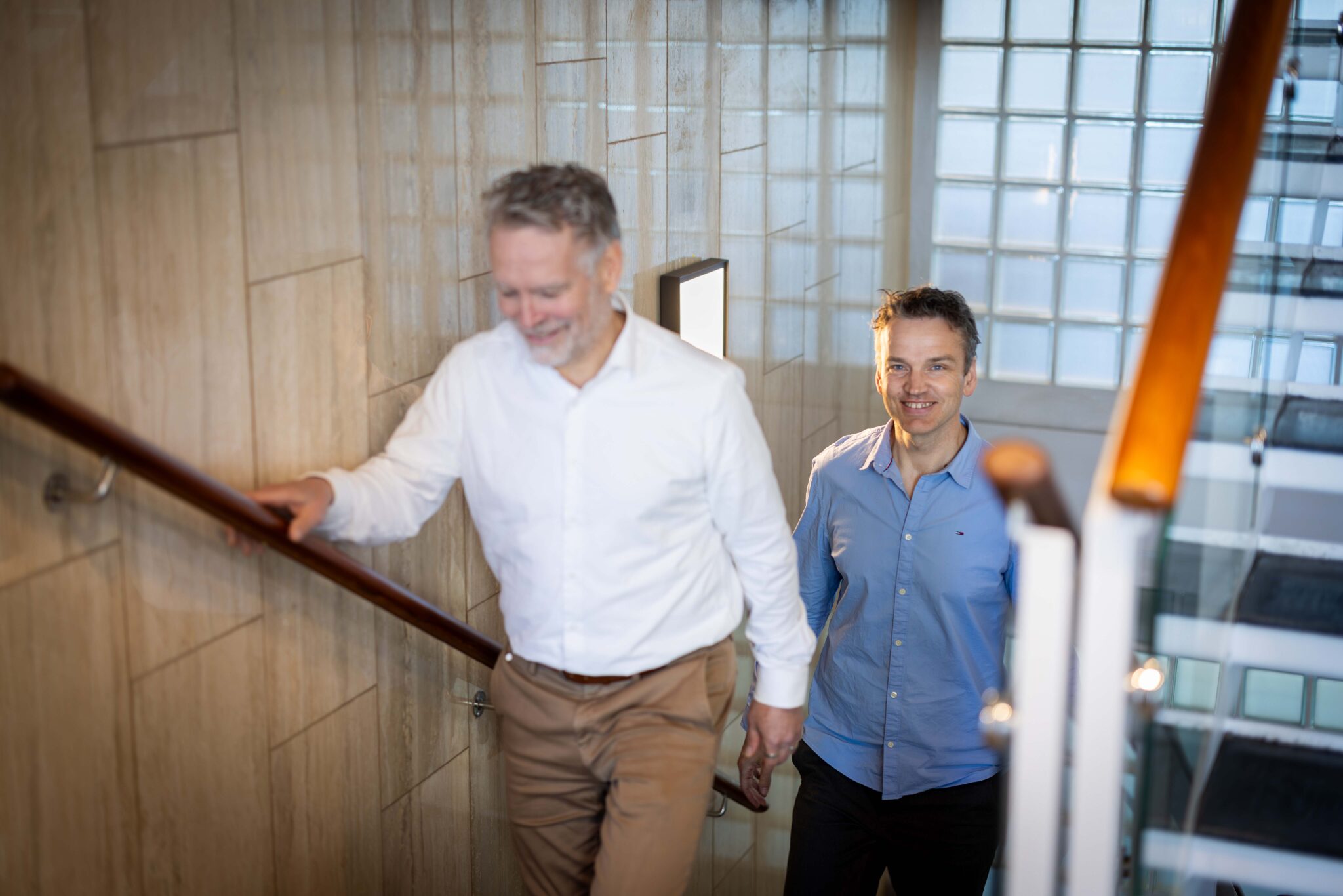To menn g&aring;r opp en trapp i et kontormilj&oslash;, med fokus p&aring; samarbeid og profesjonell arbeidshverdag