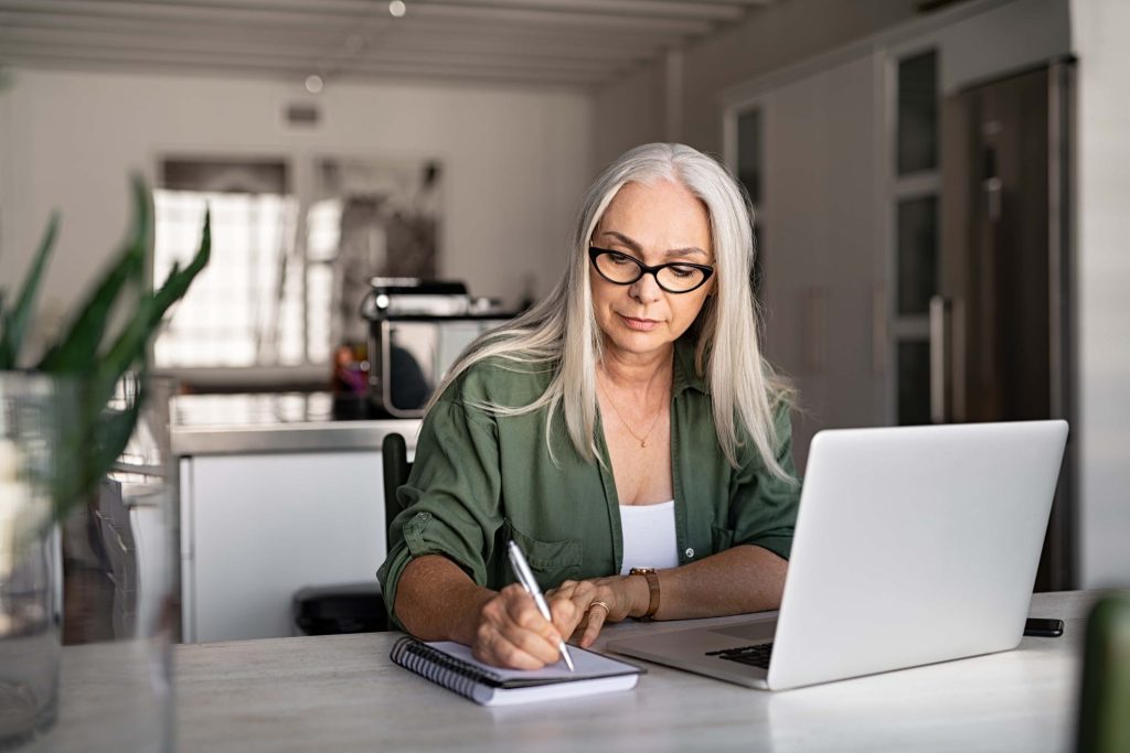 En dame sitter foran en laptop og noterer på et ark. Foto