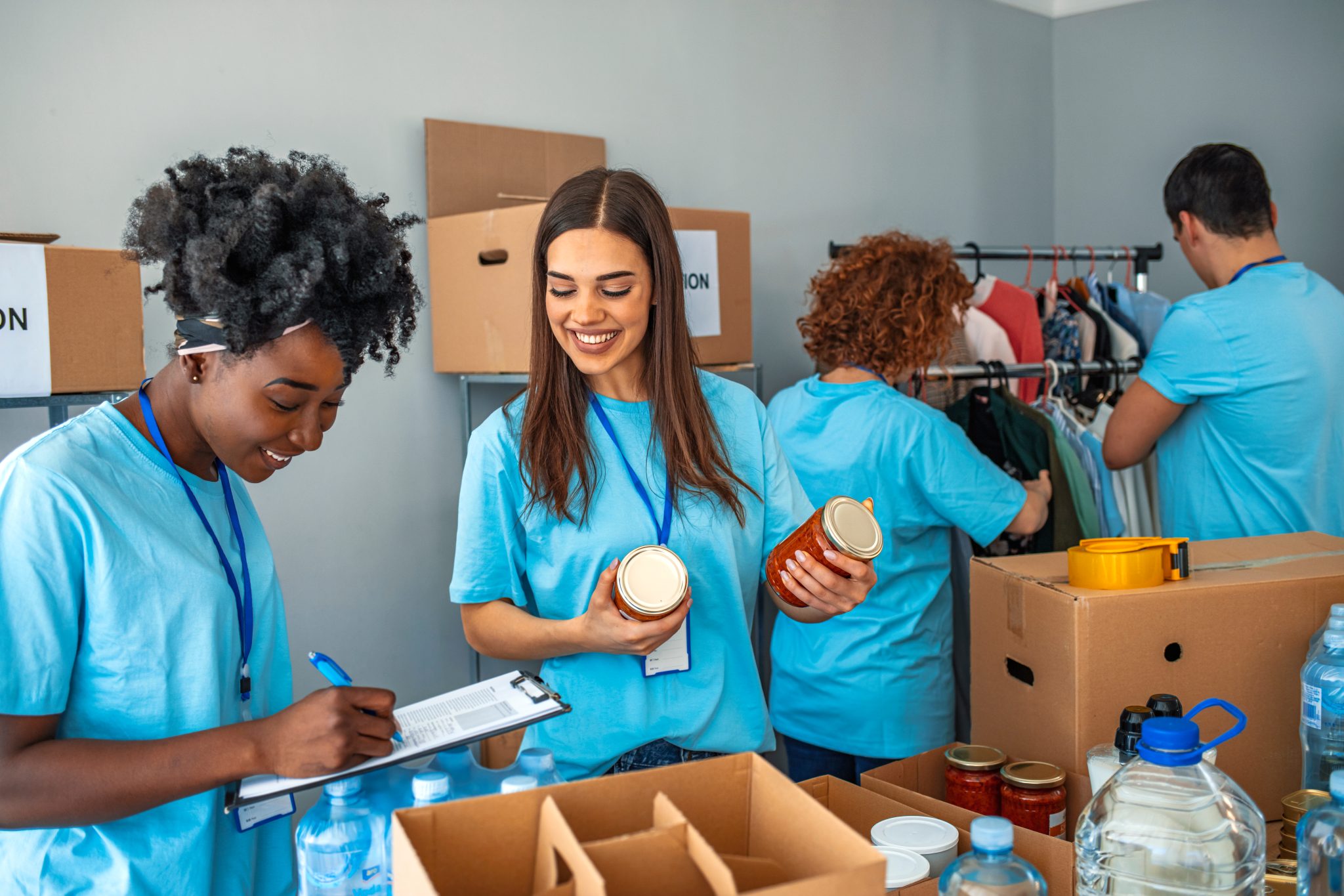 Four smiling volunteers sorting through boxes at a food bank or donation centre