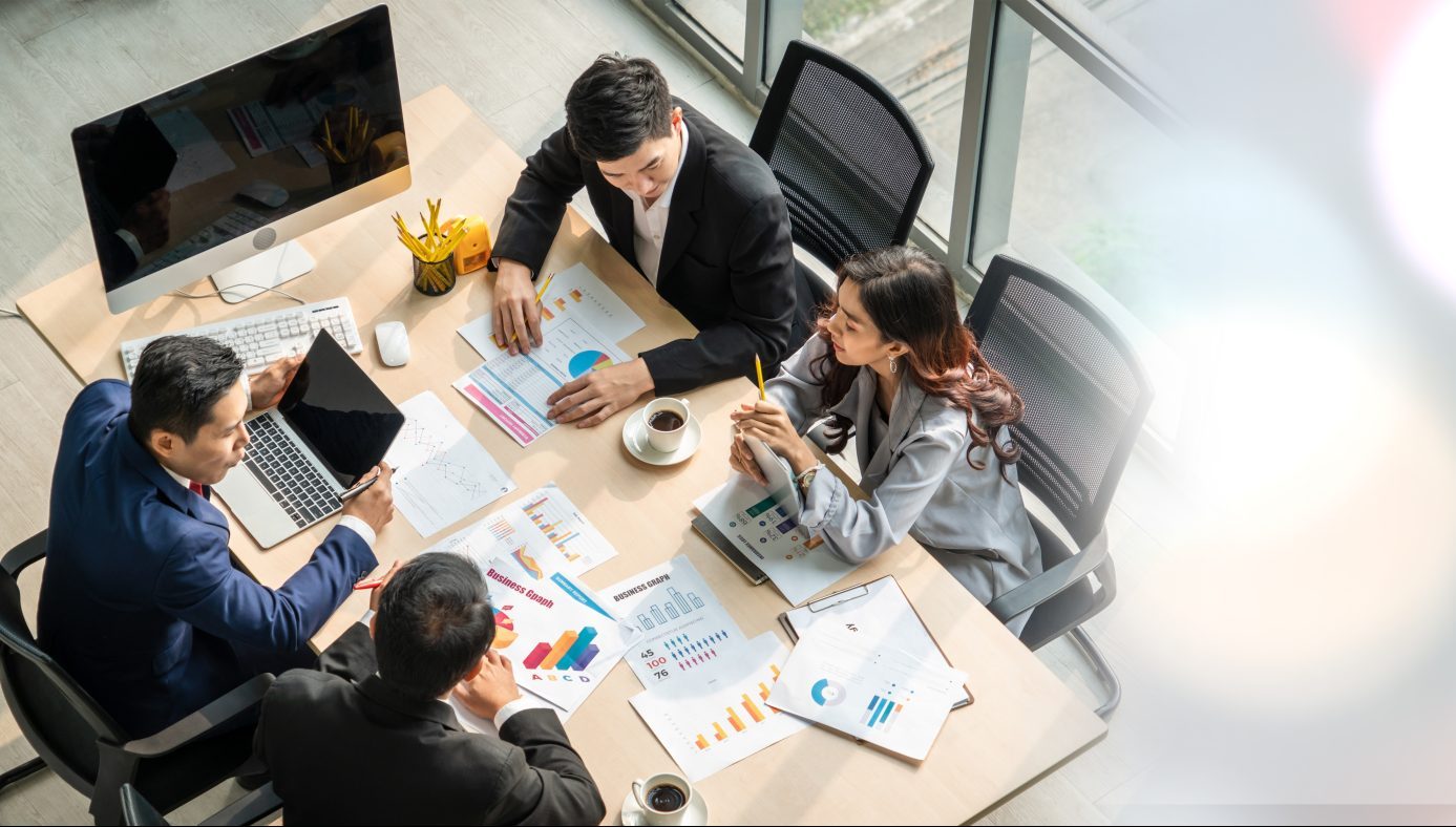 Nird's eye vie of four accountants in a brightly lit meeting room discussing finance