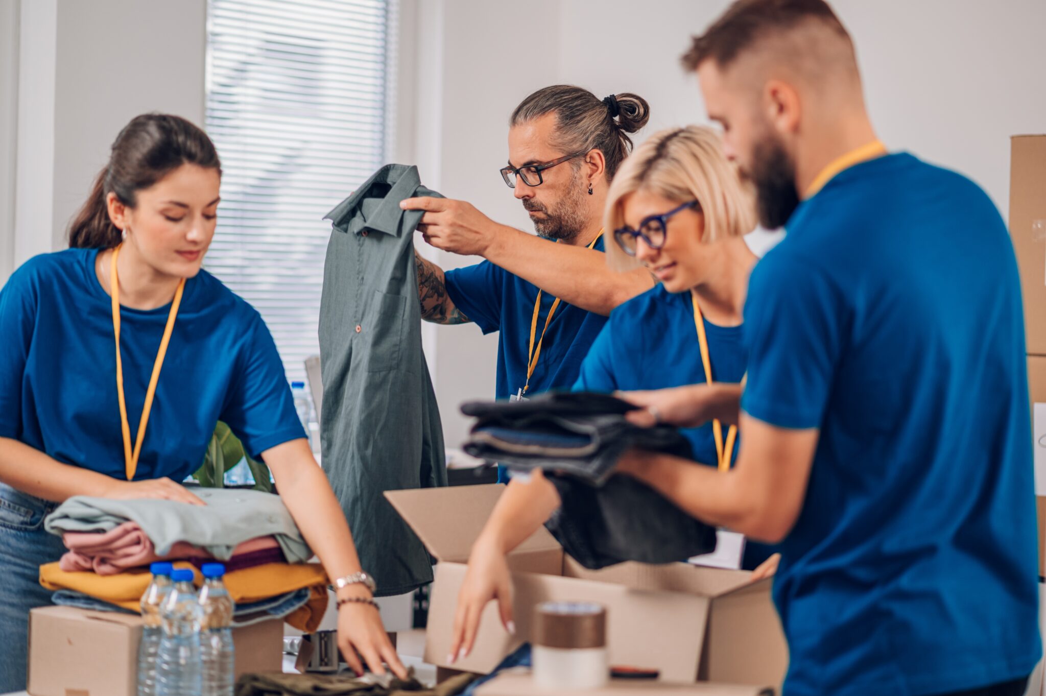 Group of diverse people working in charitable foundation. Volunteer separating donation stuff. Volunteers sort donations during food drive. Focus on a middle aged man preparing clothes.