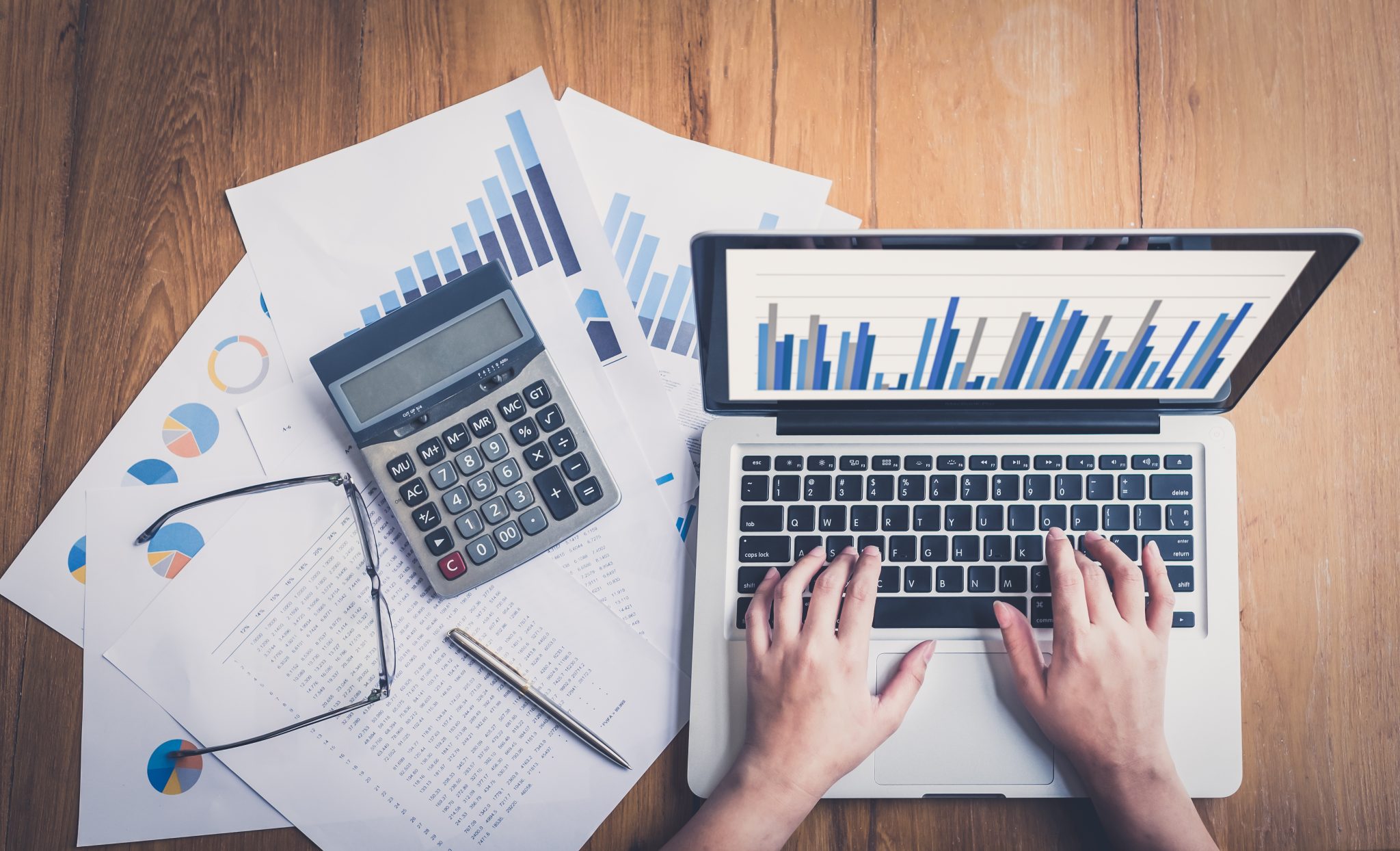 Bird's eye view of two hands working at a computer showing graphs and a calculator