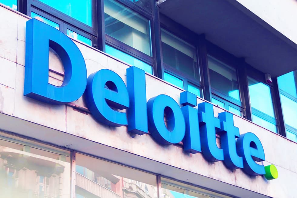 A close-up of a building façade displaying the blue “Deloitte” logo sign mounted above windows.