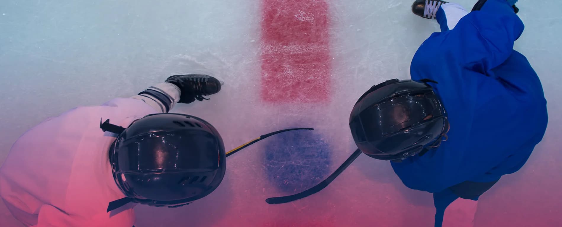 Top view of two ice hockey players facing off on the rink with sticks on the ice near a red line