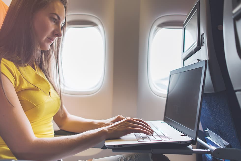 Woman working on a laptop while seated on an airplane.
