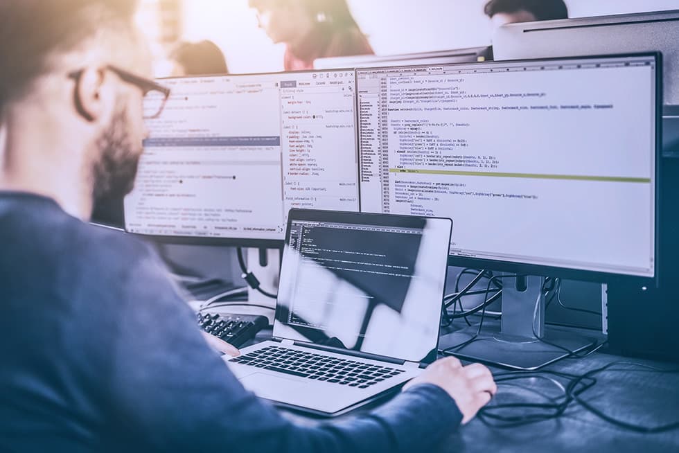 Developer working on code using a laptop and multiple monitors