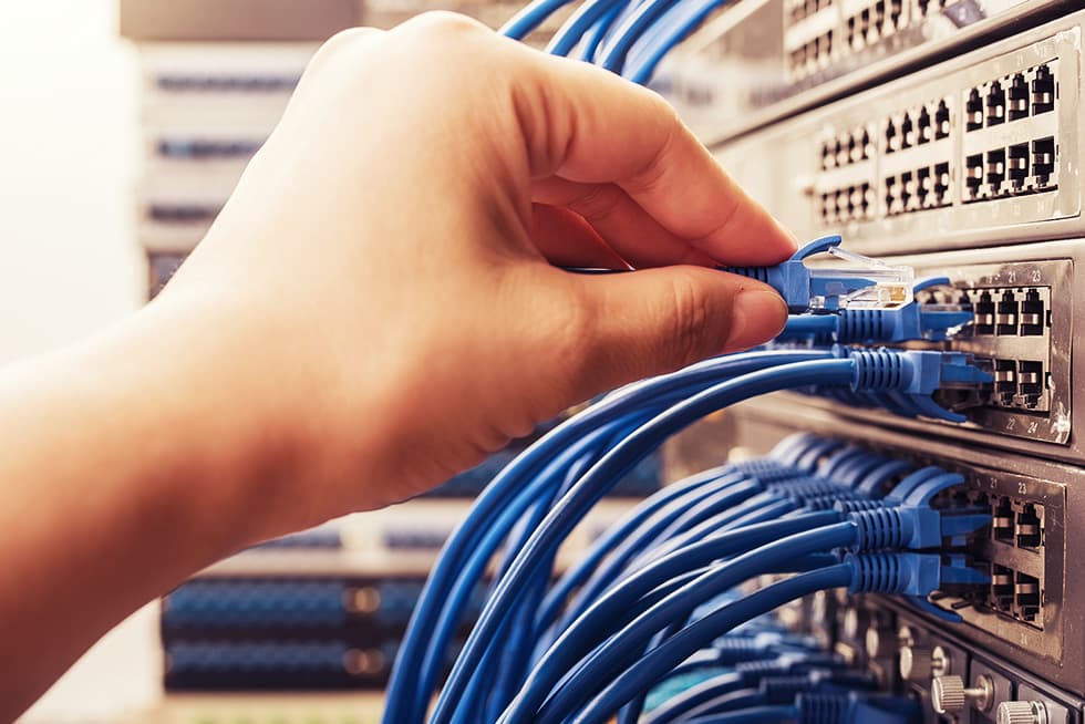 Hand plugging an Ethernet cable into a network switch in a server rack