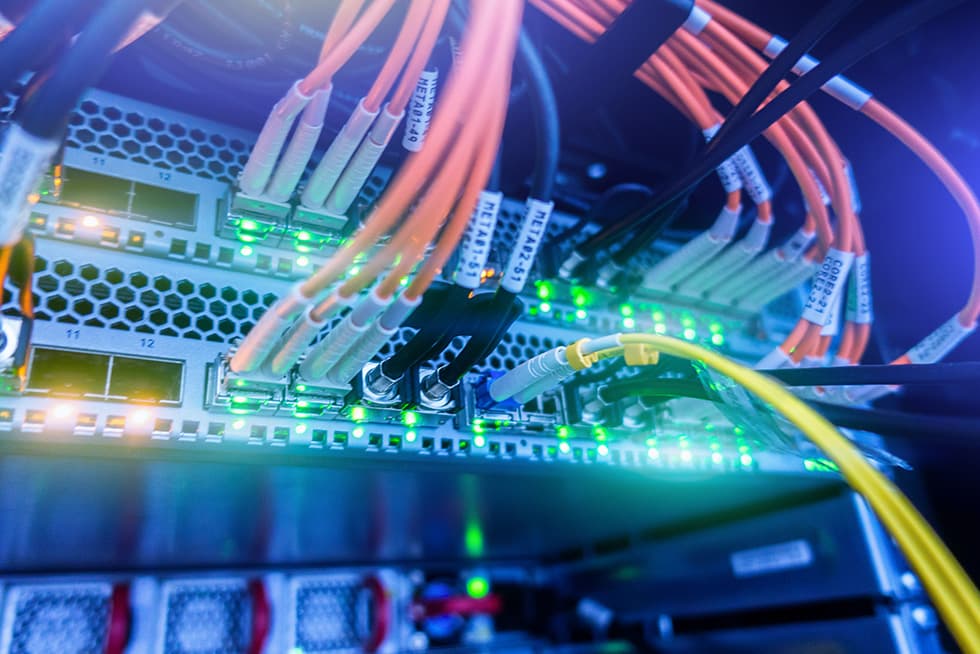 A close-up of network switches in a server rack with multiple connected Ethernet cables and green status lights blinking.