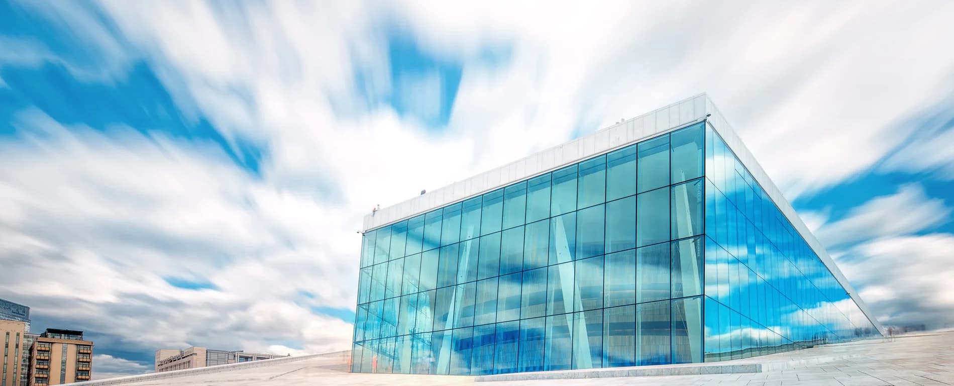 Modern glass facade of the Oslo Opera House under a cloudy sky