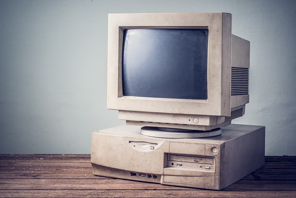 An old beige desktop computer with a bulky CRT monitor sitting on a wooden table against a plain wall.