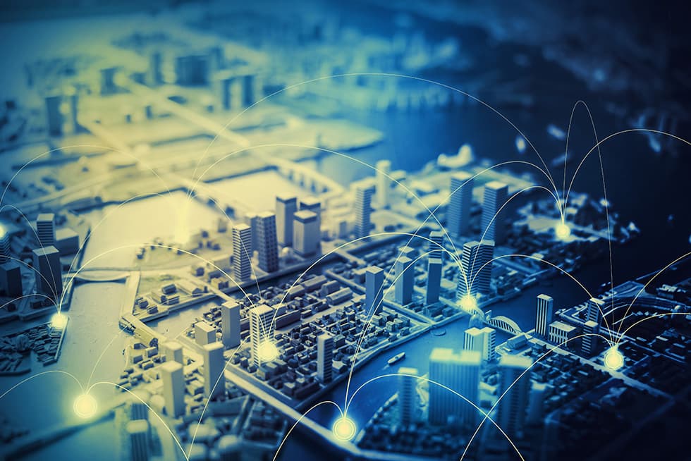 A stylized miniature cityscape with glowing connection points and curved lines linking different buildings, representing a smart city or digital network infrastructure.