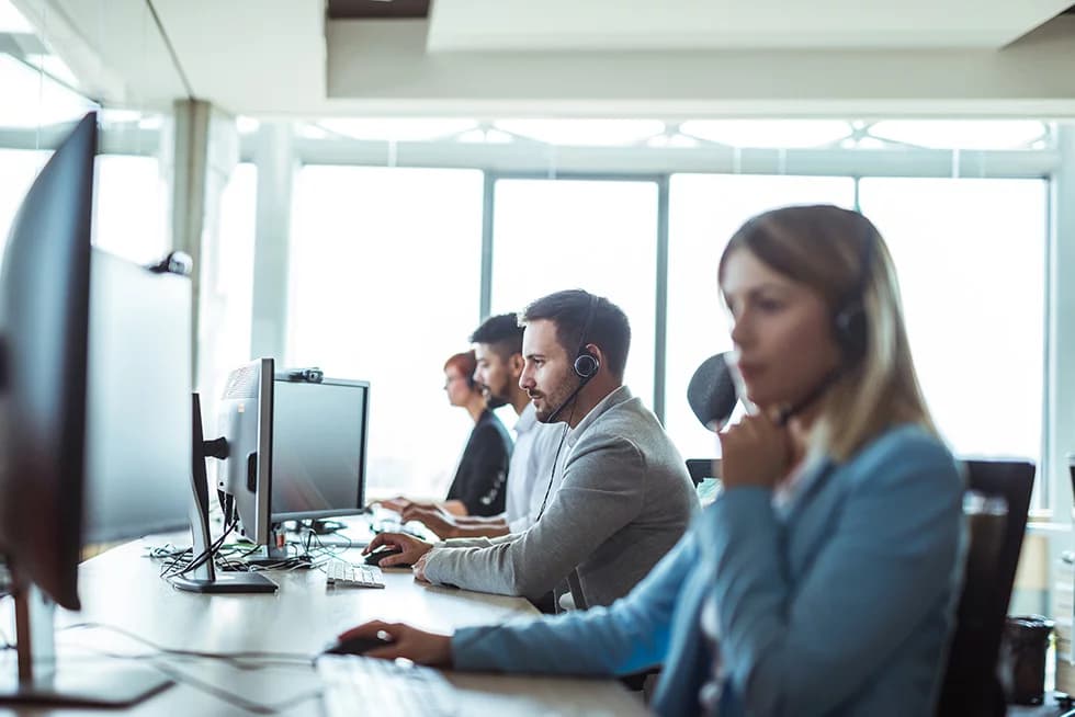 Customer support team wearing headsets working at computers in a modern office.