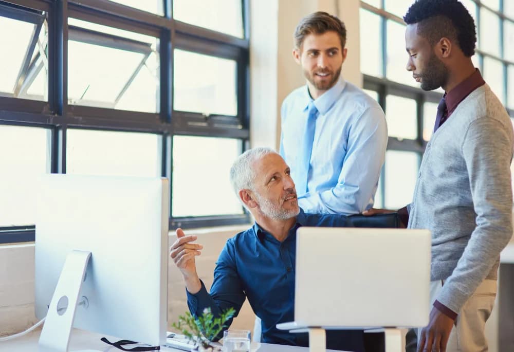 Three business colleagues discussing work together around a desk in a modern office.