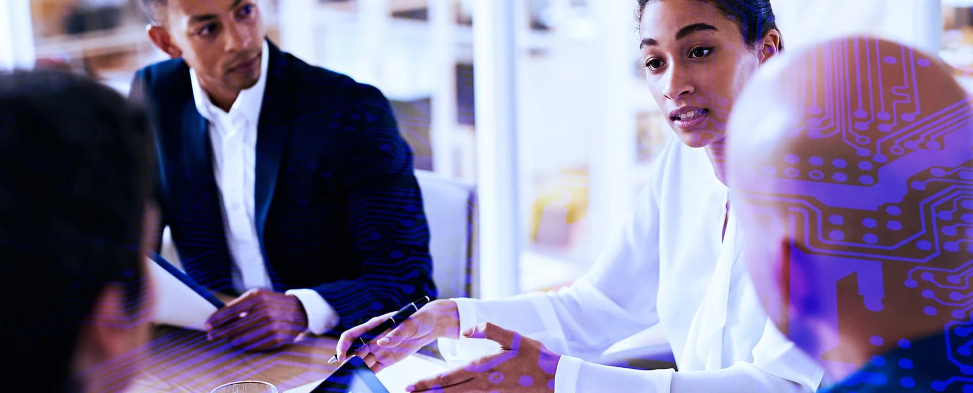 A group of professionals sit in a meeting, with a woman speaking and holding a pen while others listen, overlaid with digital circuit patterns suggesting a technology-focused discussion.