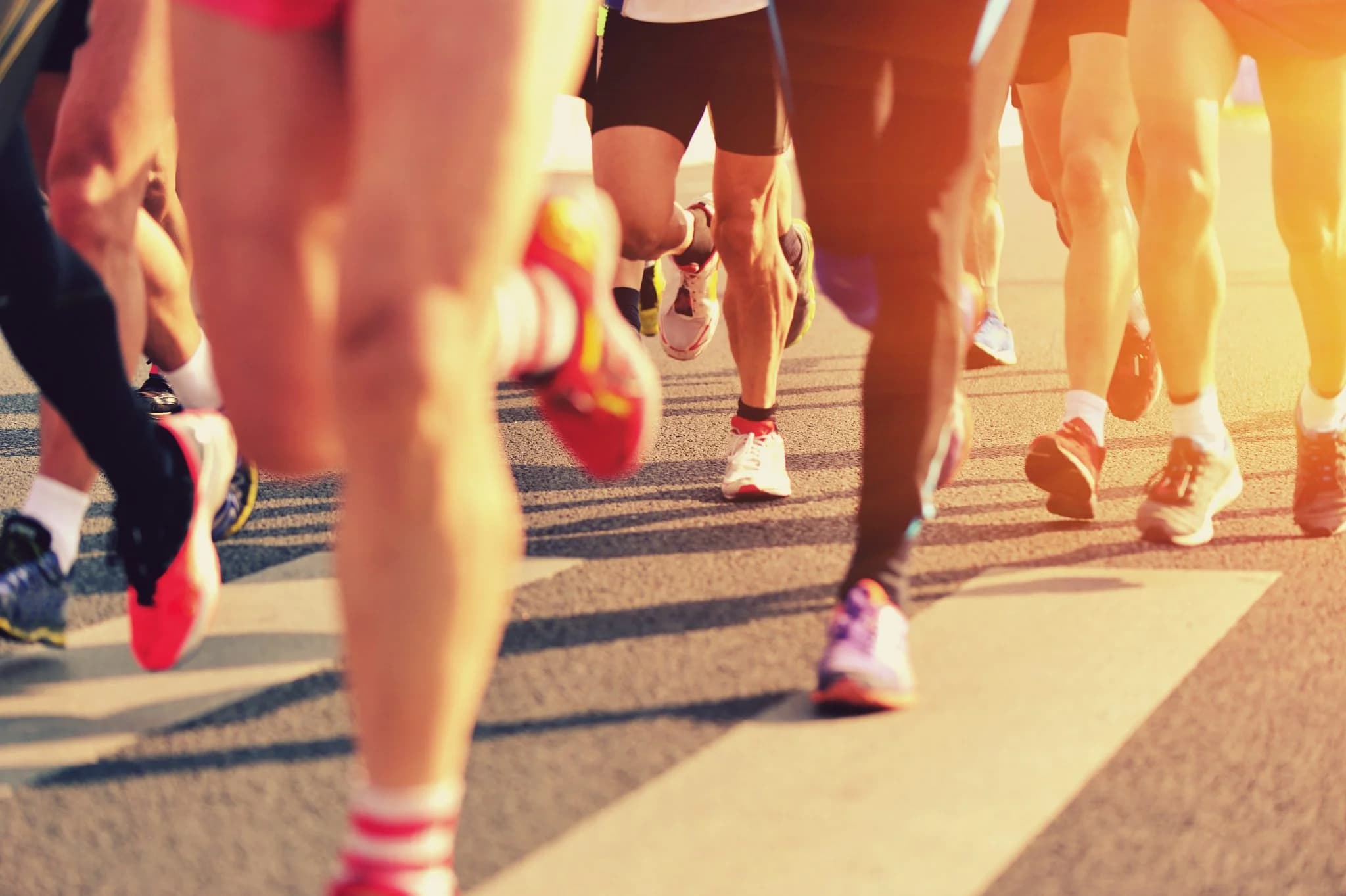 Close-up of runners’ legs and colorful sneakers during a road race in warm sunlight.