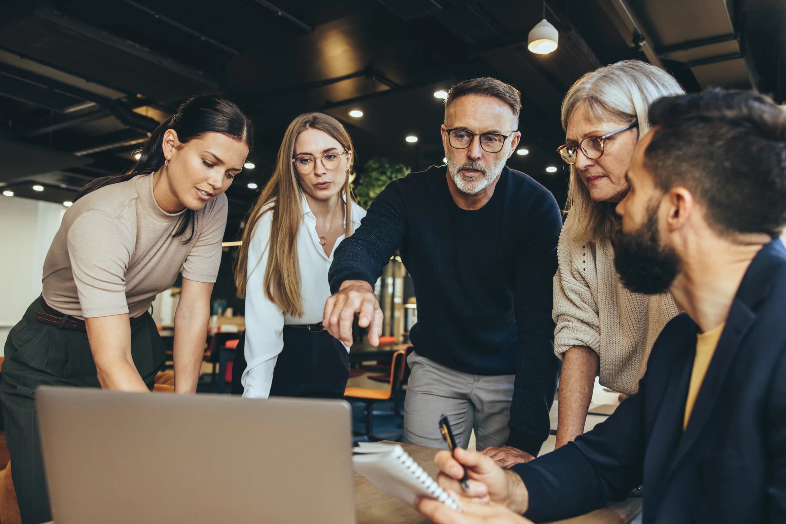 Team of colleagues gathered around a laptop, discussing and reviewing information together in an office.