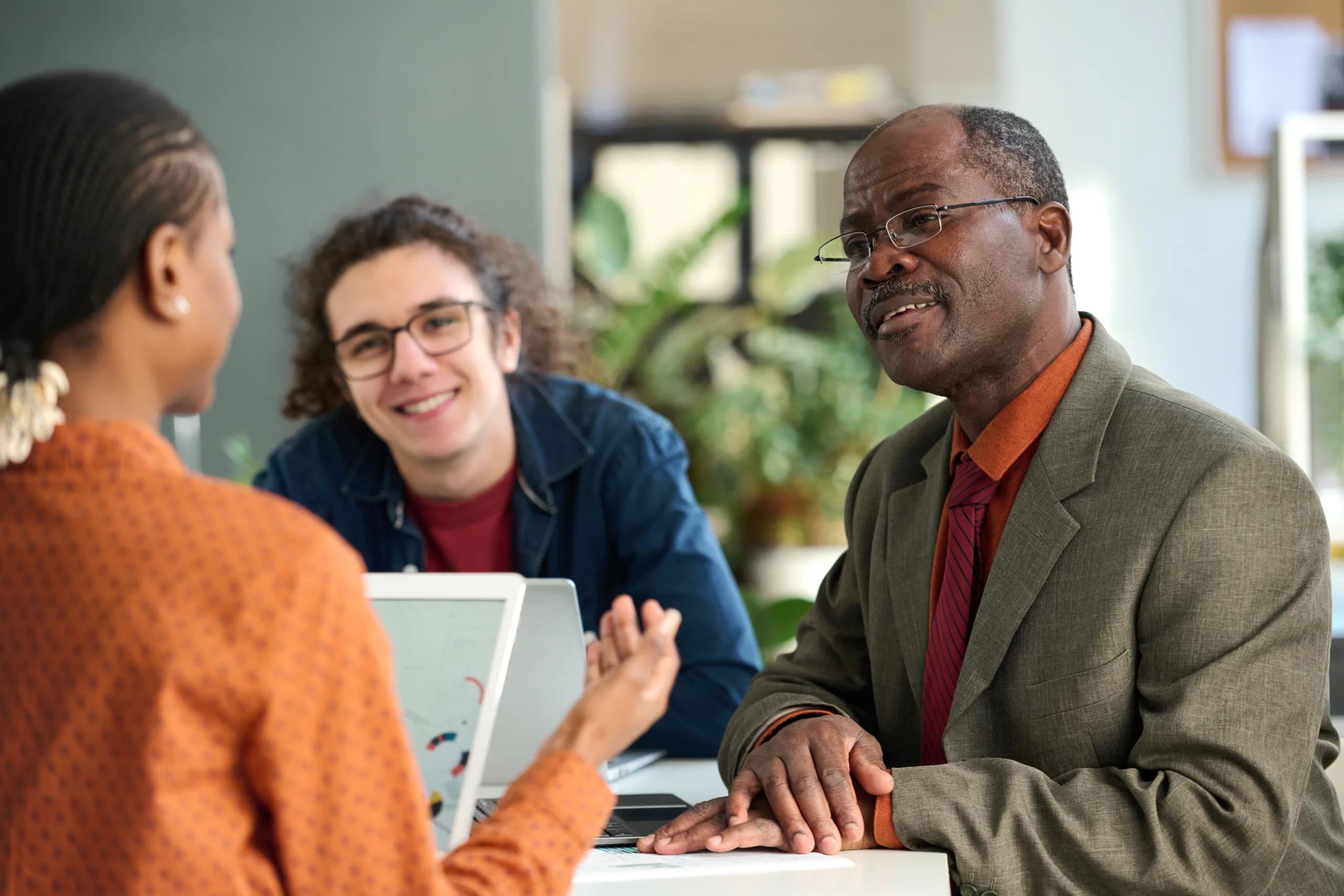 Two colleagues discussing with a client at a desk, with a laptop open during a meeting.