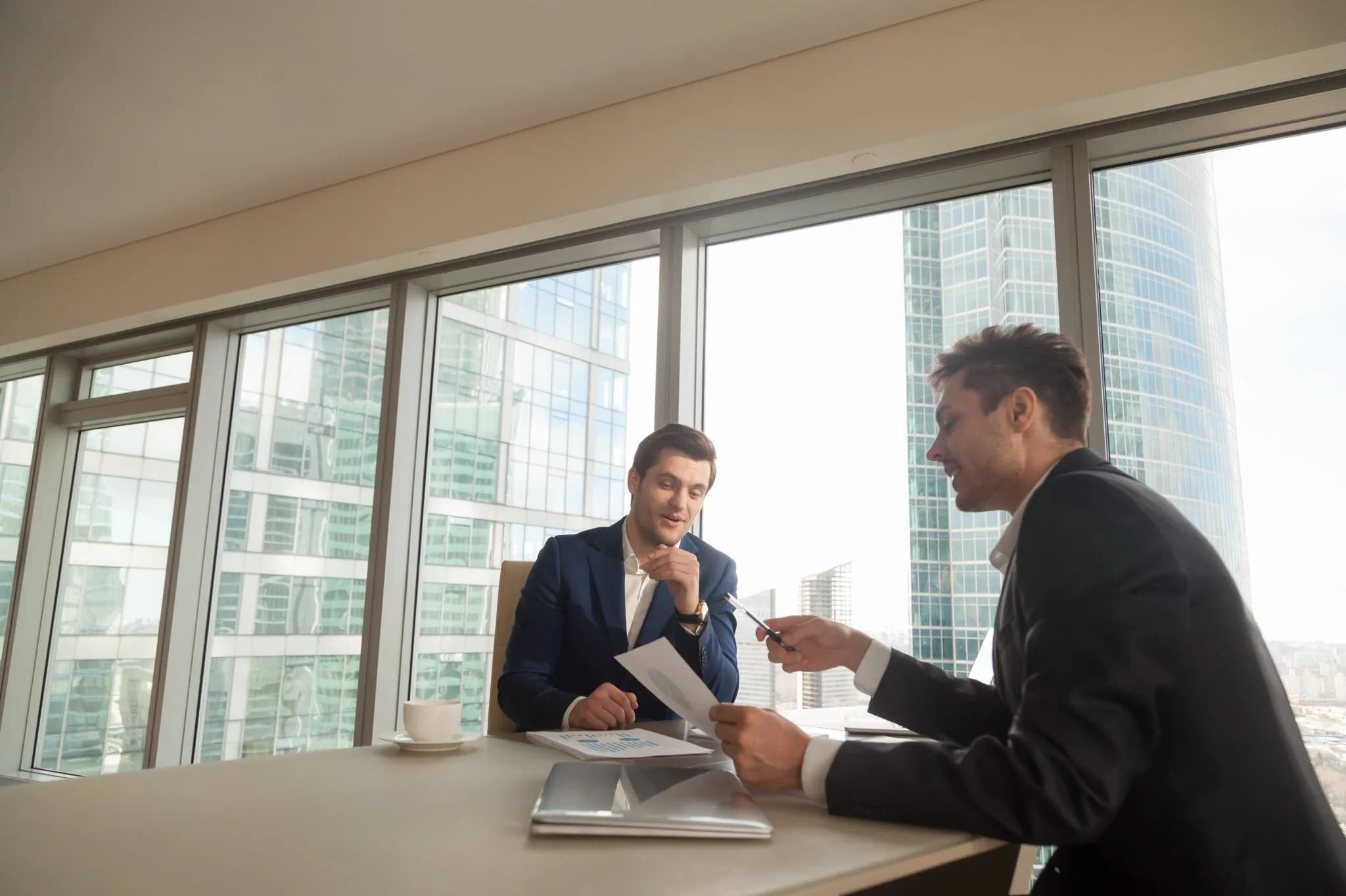 Two business professionals discussing documents in an office with city view