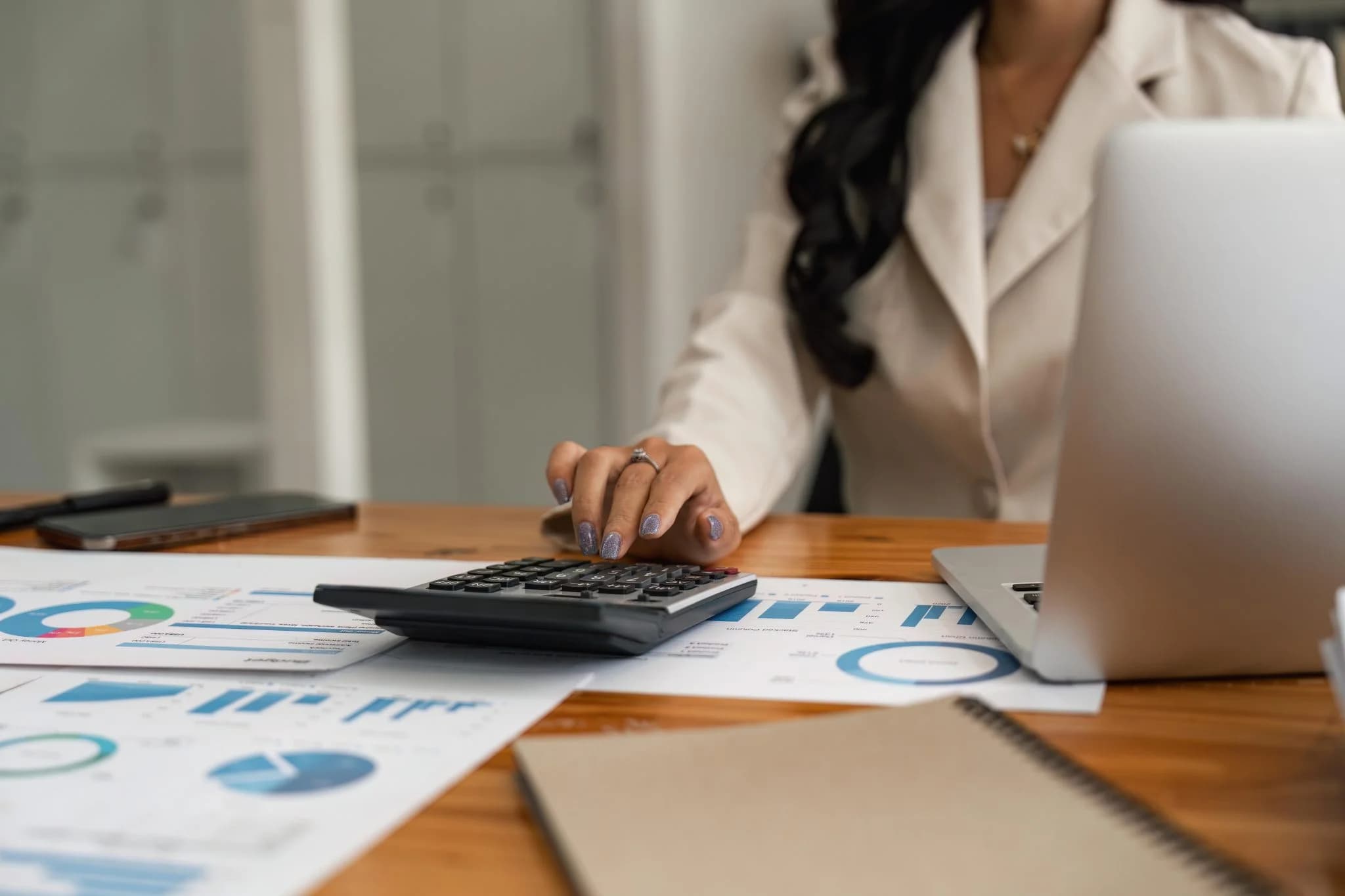 Person using a calculator with financial reports and laptop on a desk