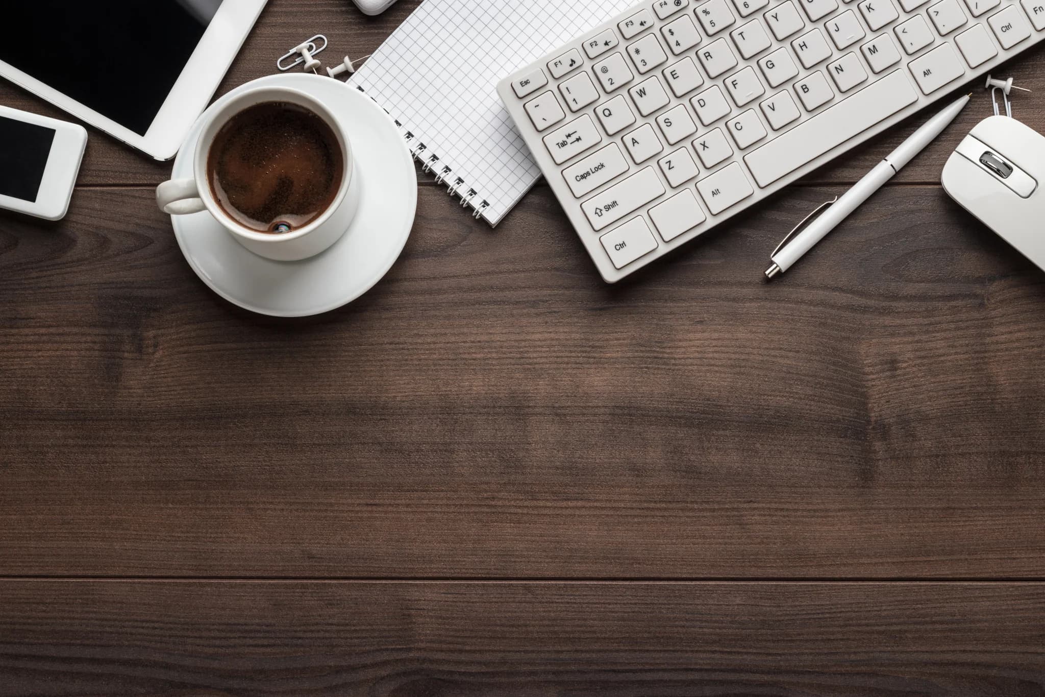 Workspace with coffee, keyboard, notebook, and devices on a wooden desk