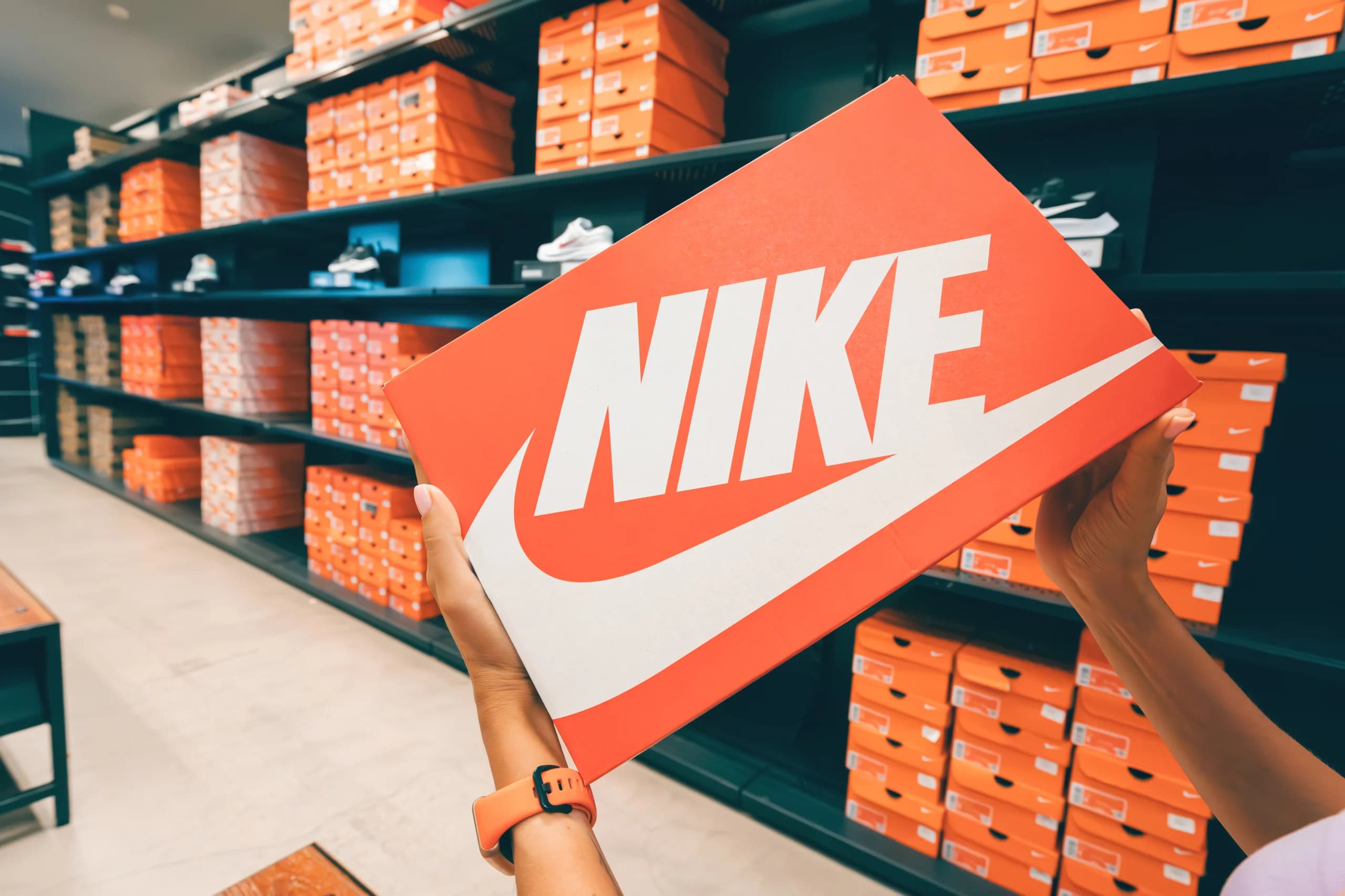 Person holding a Nike shoebox in a store with shelves of shoe boxes