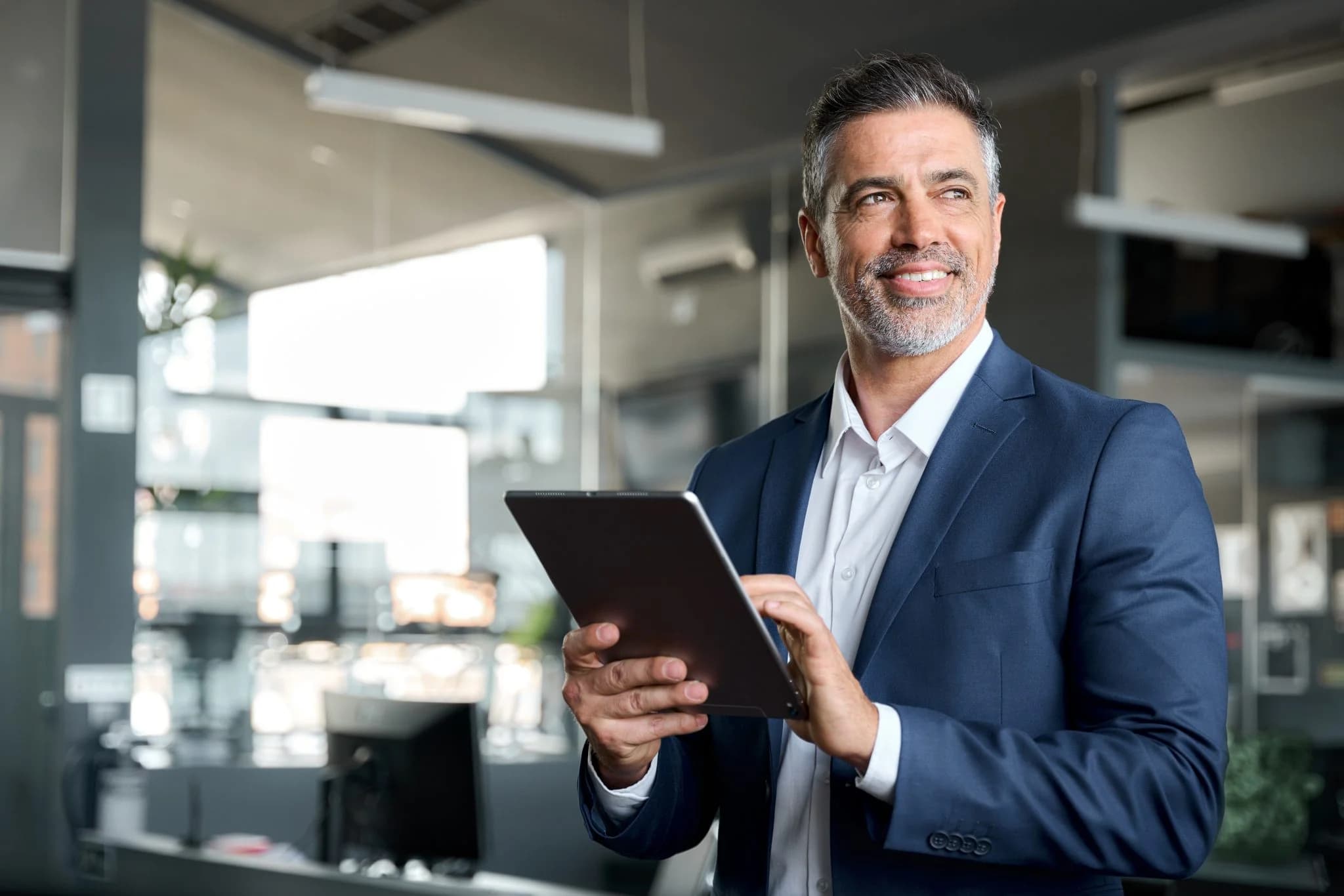 Smiling businessman in a suit using a tablet in a modern office.