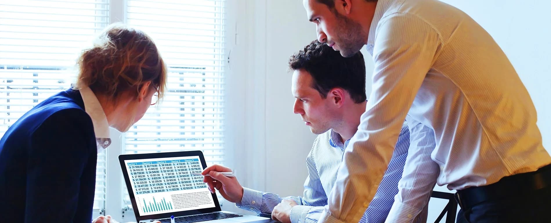Three colleagues reviewing data on a laptop screen together.