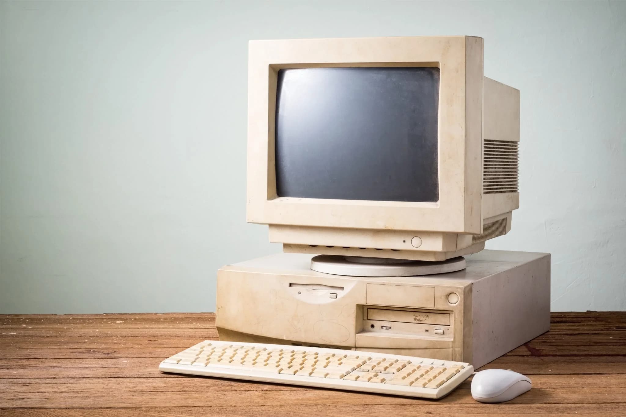 Old desktop computer with monitor, keyboard, and mouse on a wooden desk.