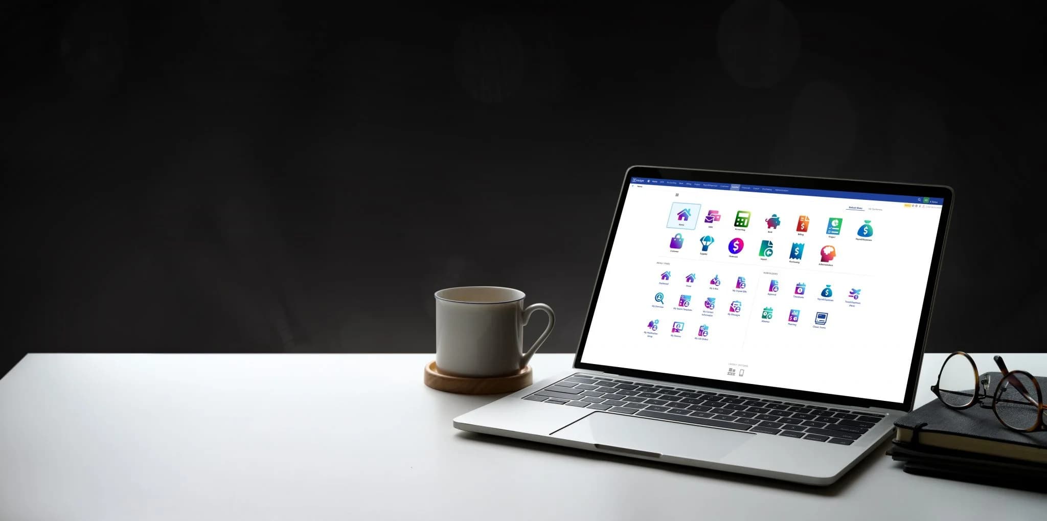 A laptop on a desk displaying the Xledger dashboard with various application icons, next to a coffee mug and a notebook with glasses, set against a dark background.