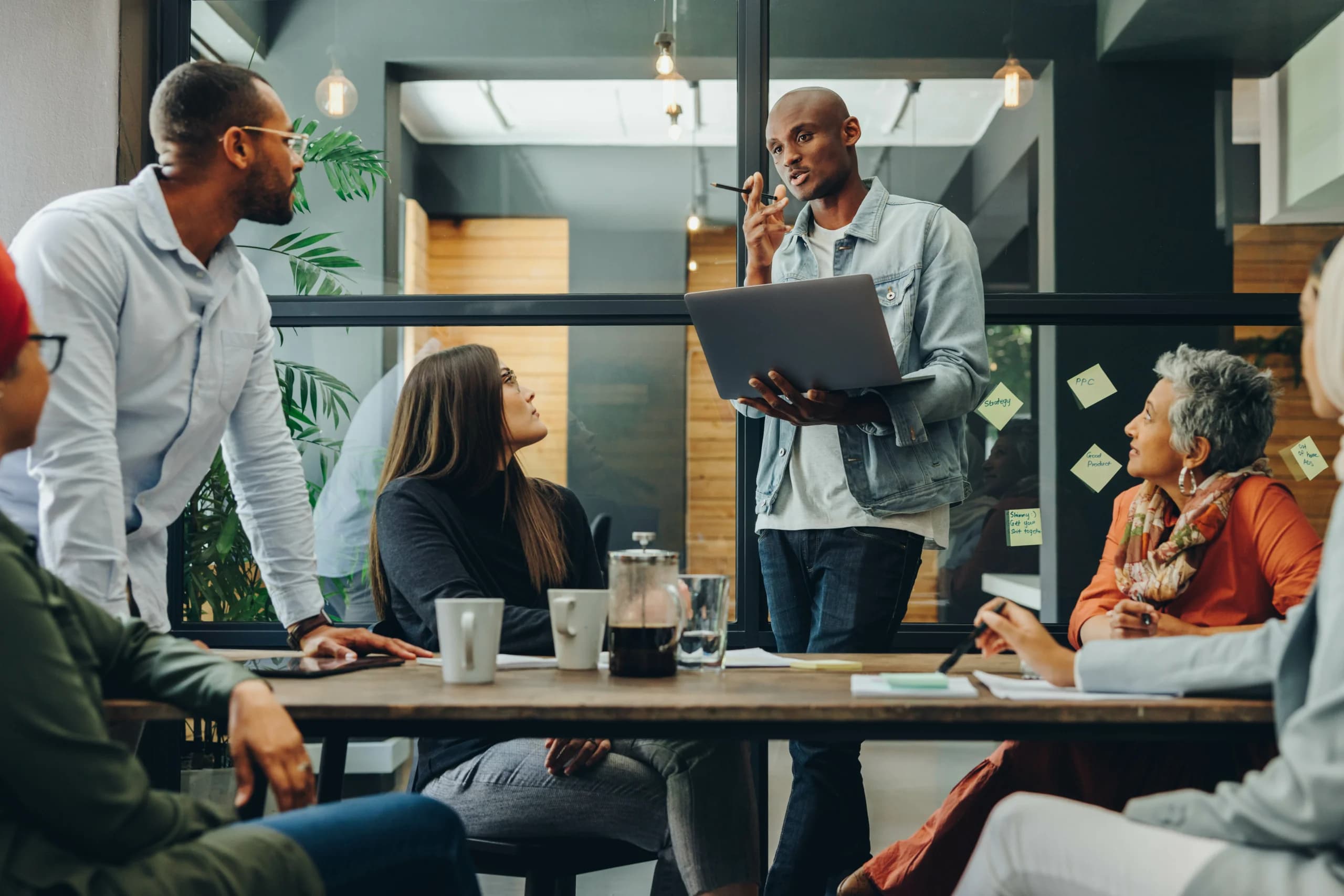 Man presenting ideas with a laptop to a diverse team during a meeting in a modern office.