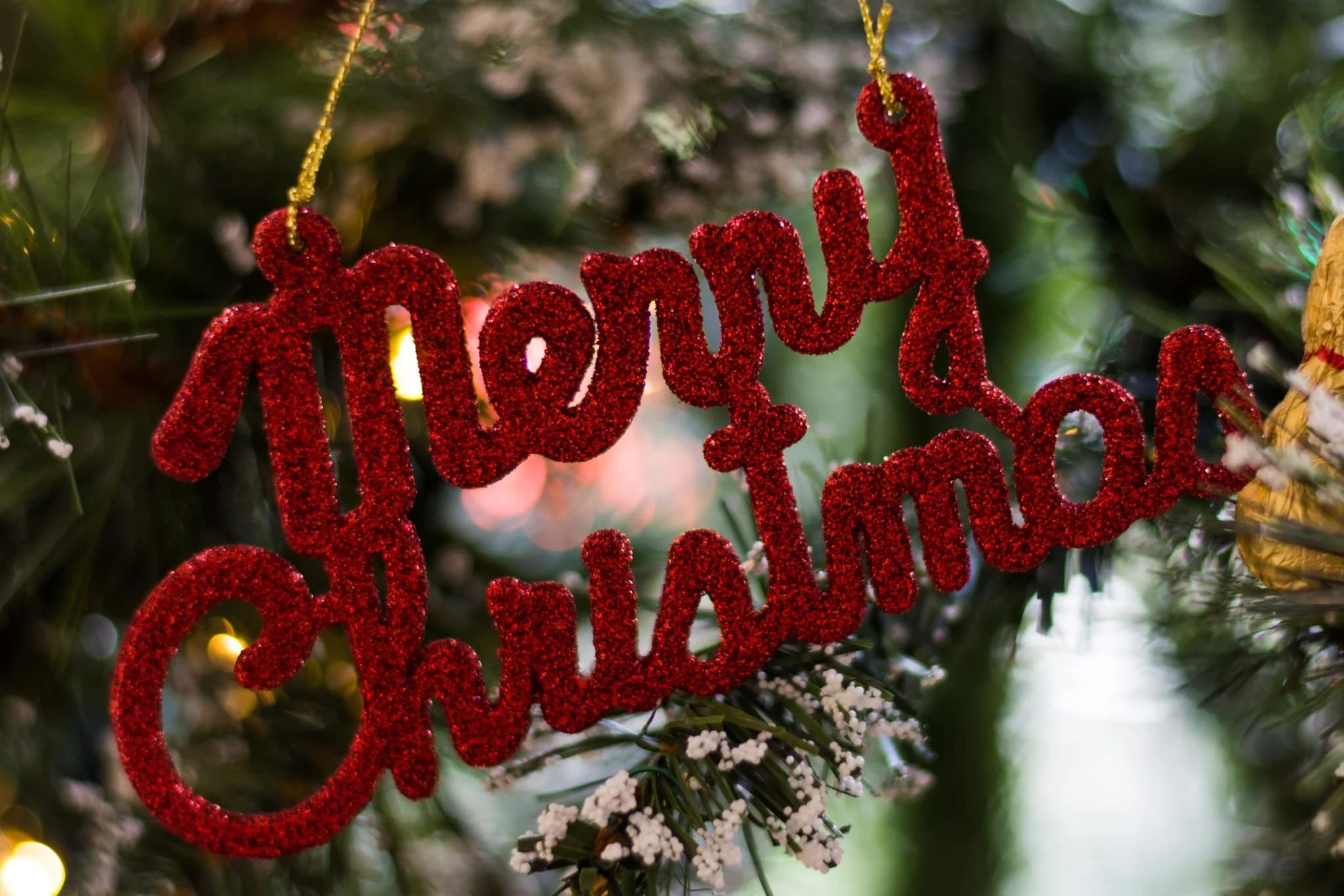 Red glitter “Merry Christmas” ornament hanging on a decorated Christmas