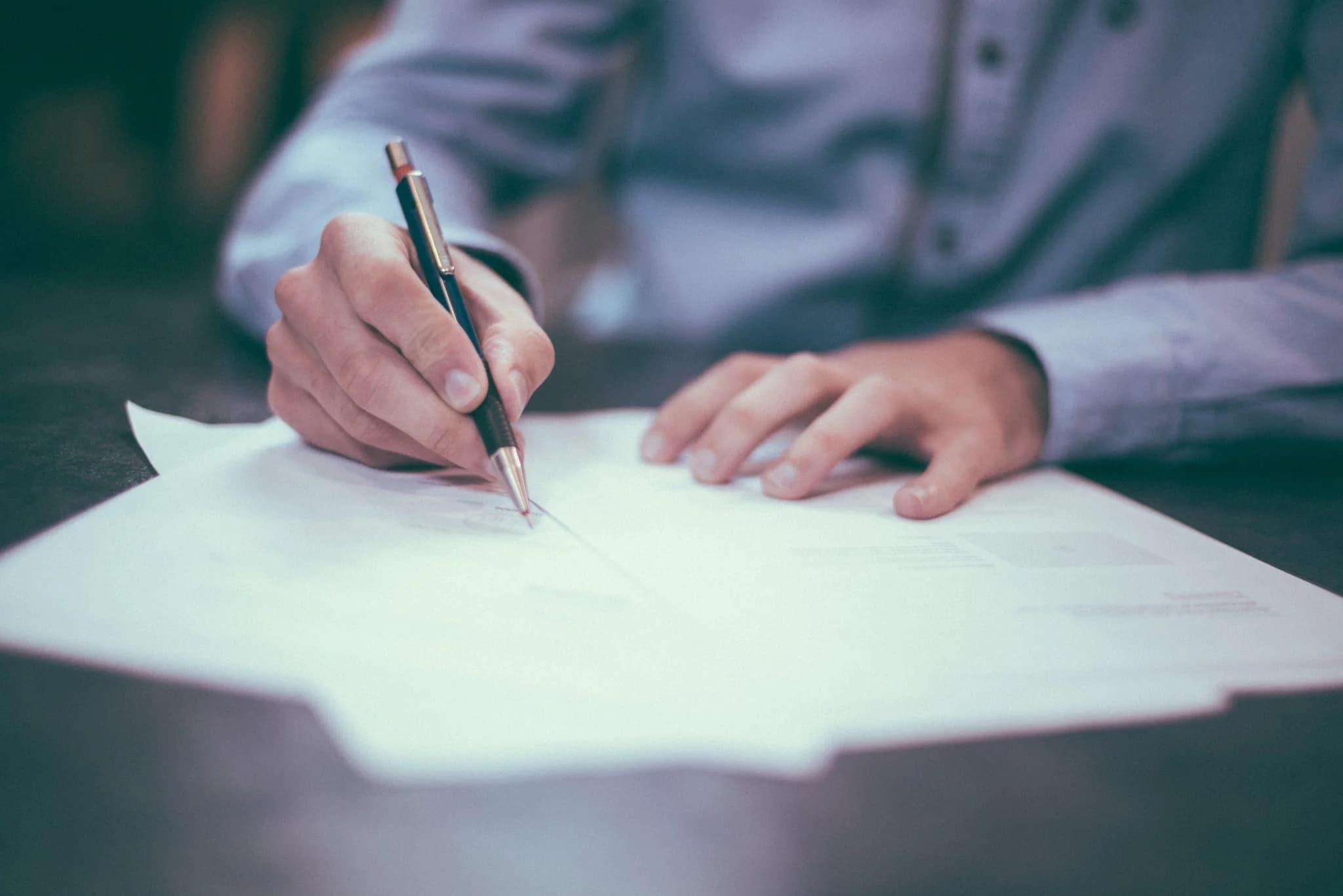Close-up of a person signing a document with a pen on a desk.