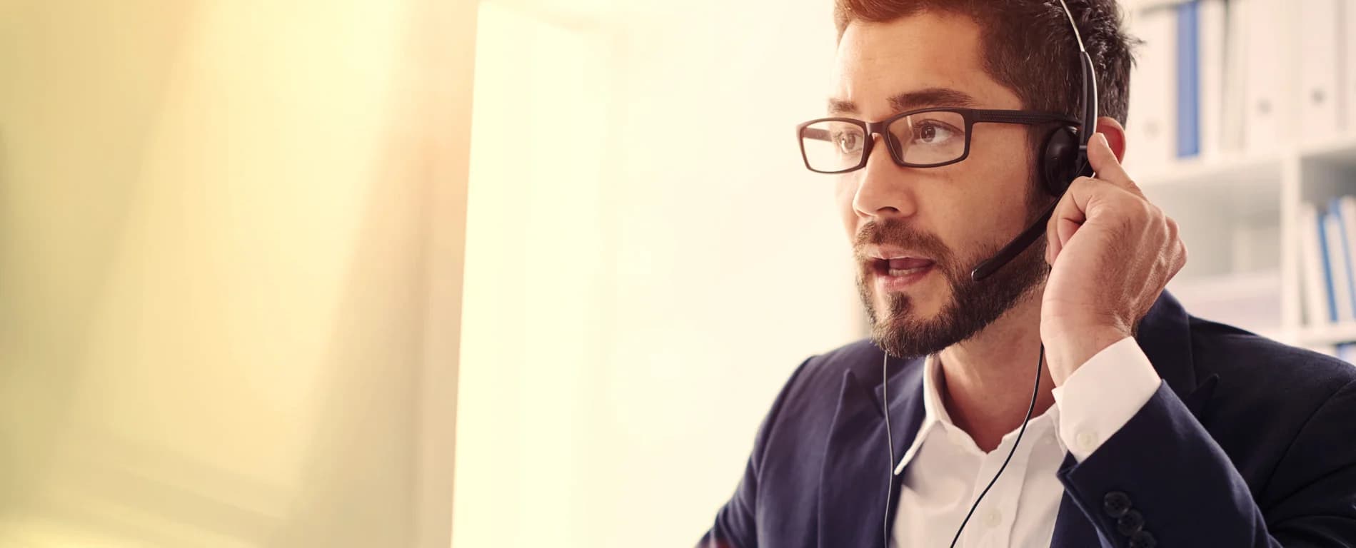 Man wearing a headset speaking while working at a computer, representing customer support or a call center agent.