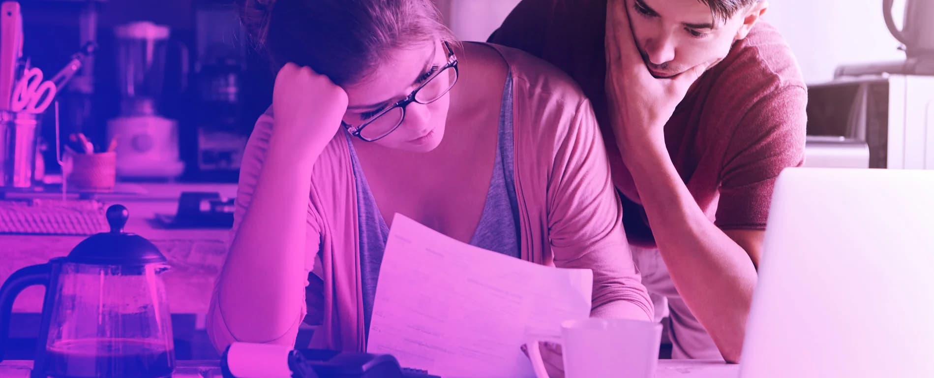 Couple reviewing bills and documents with a laptop at home, appearing concerned about finances.