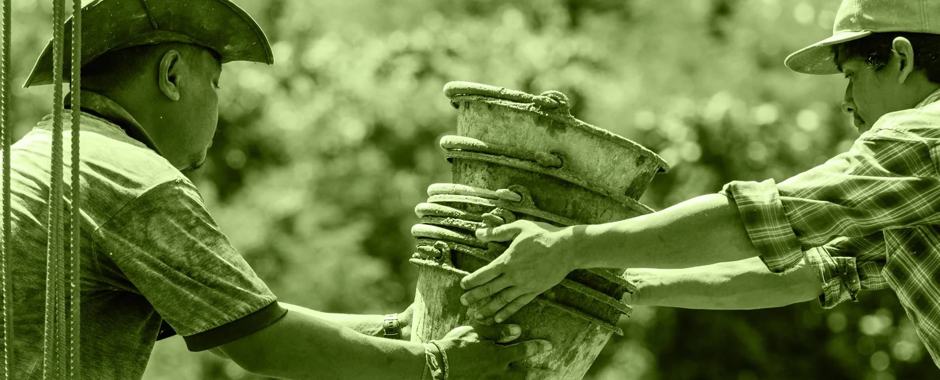 Two workers wearing hats pass a stack of buckets between each other outdoors, tinted in green