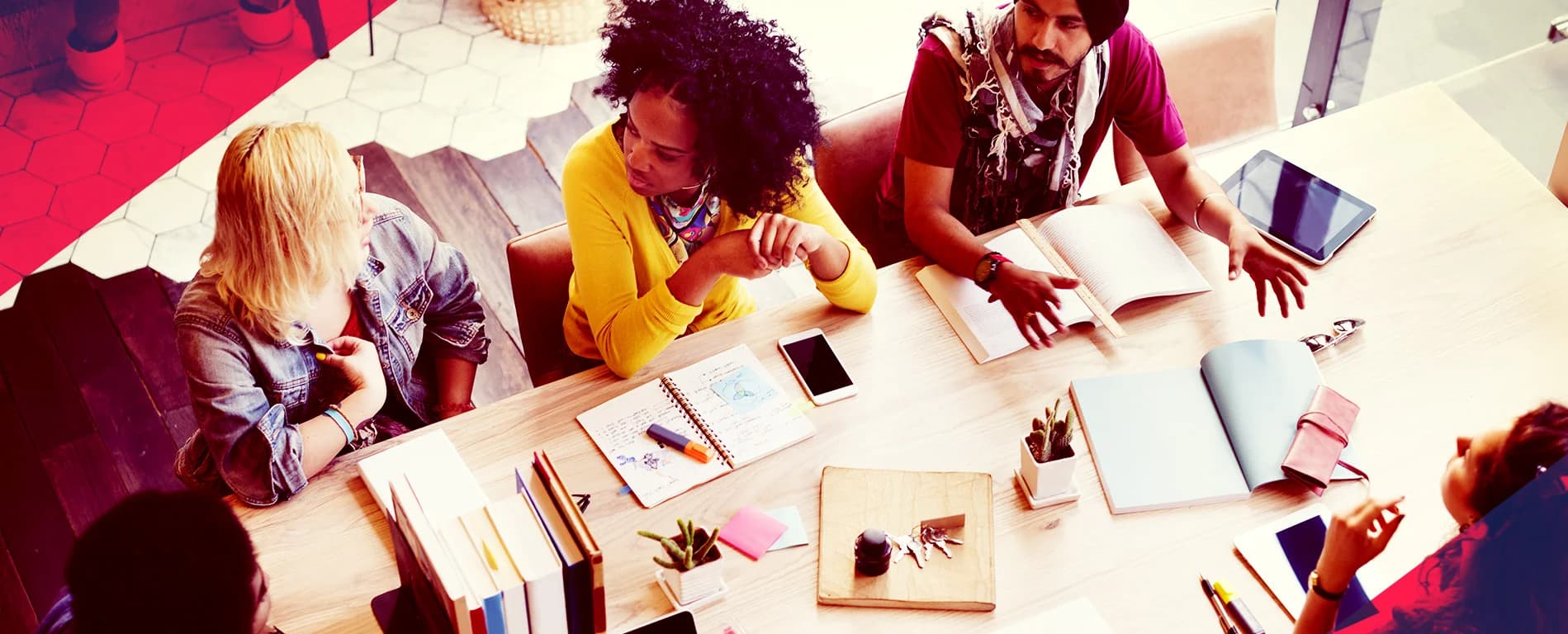 Diverse group of colleagues collaborating around a table with notebooks, books, and digital devices in a modern workspace
