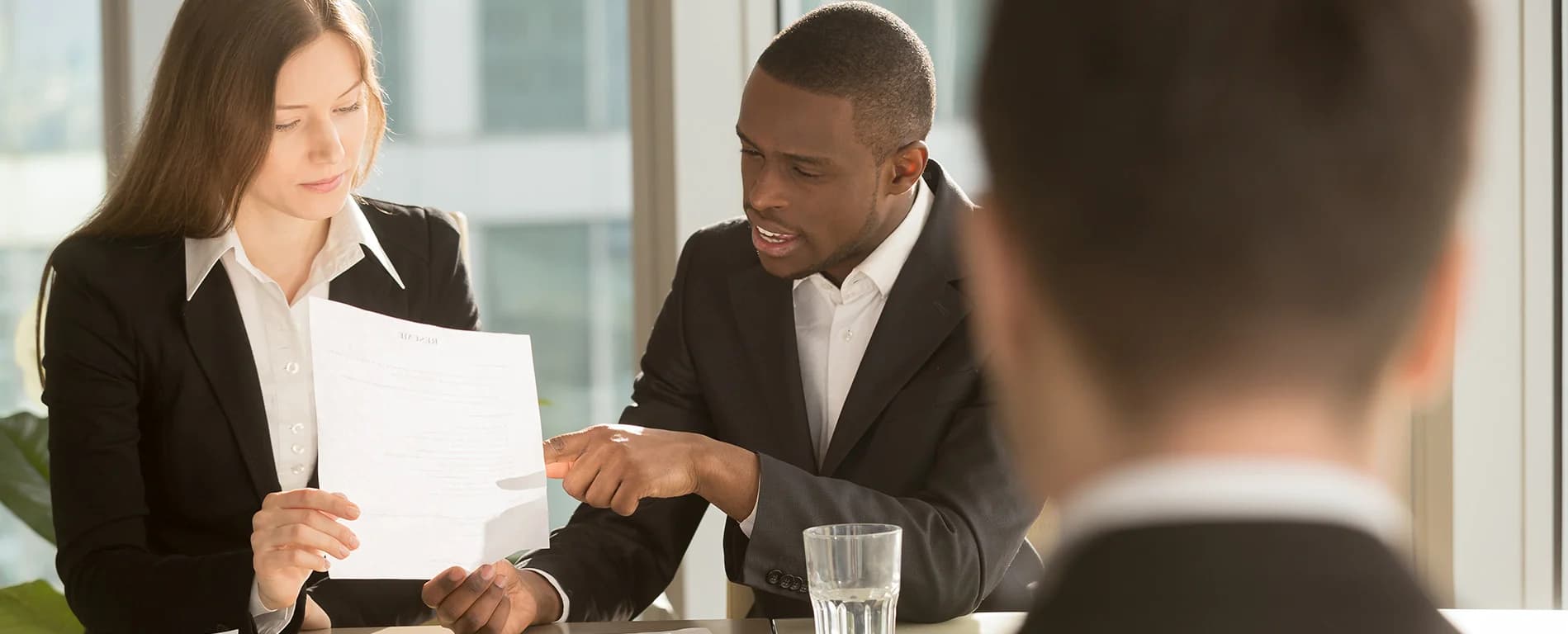 Two business professionals reviewing a document together at a table during a meeting in a bright office