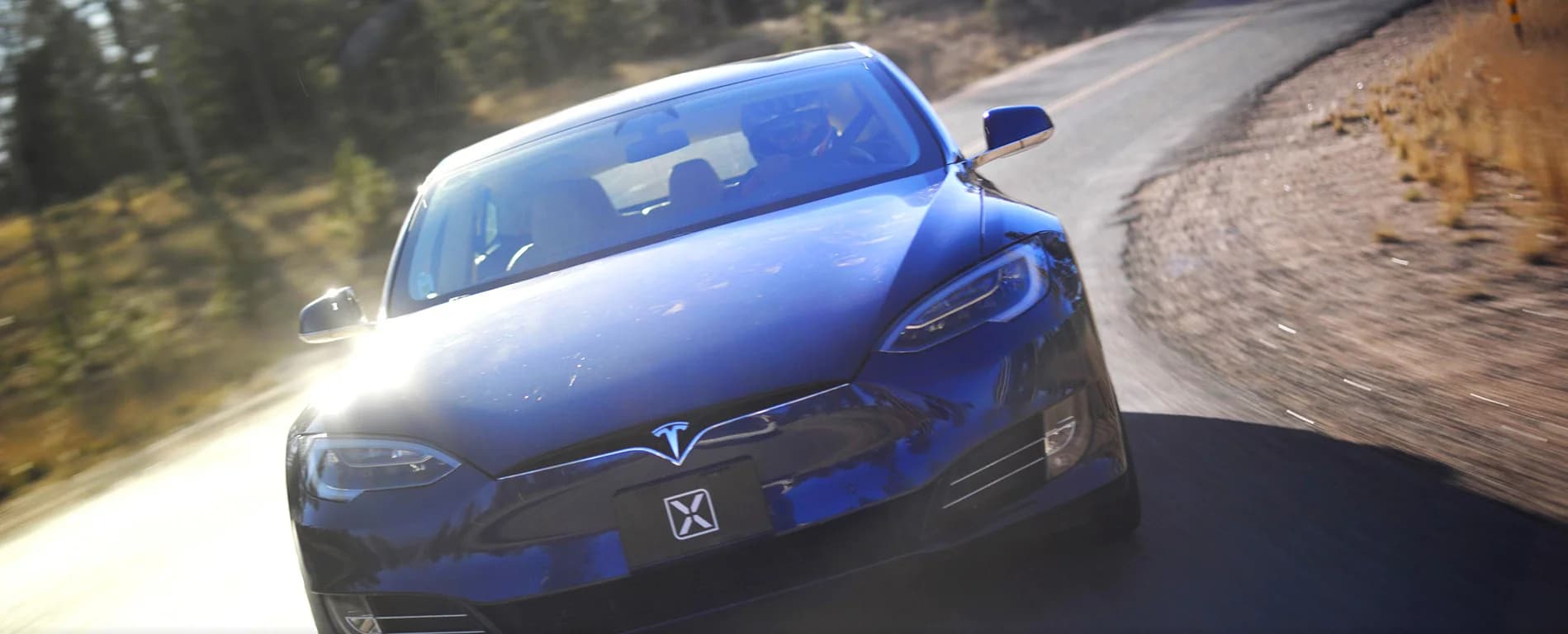 Blue electric car driving on a winding road in a forest.
