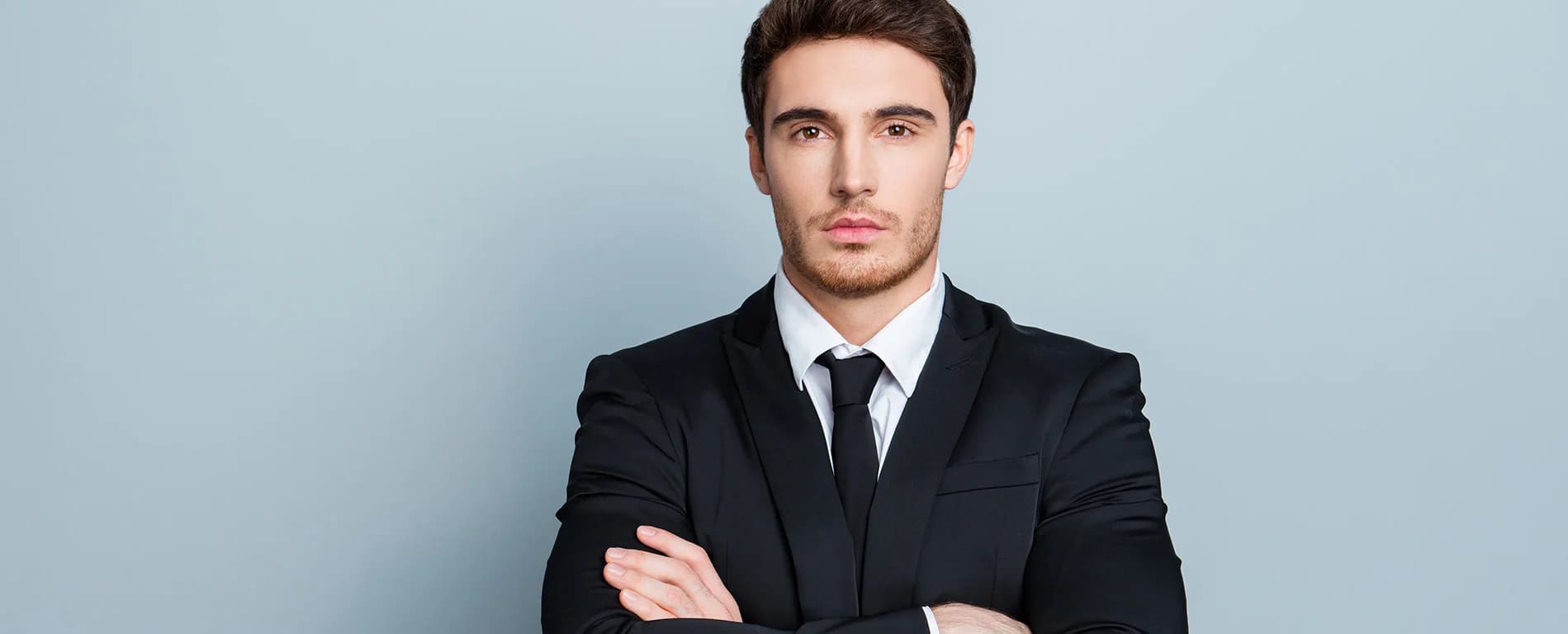 Man in a black suit with arms crossed, looking at the camera
