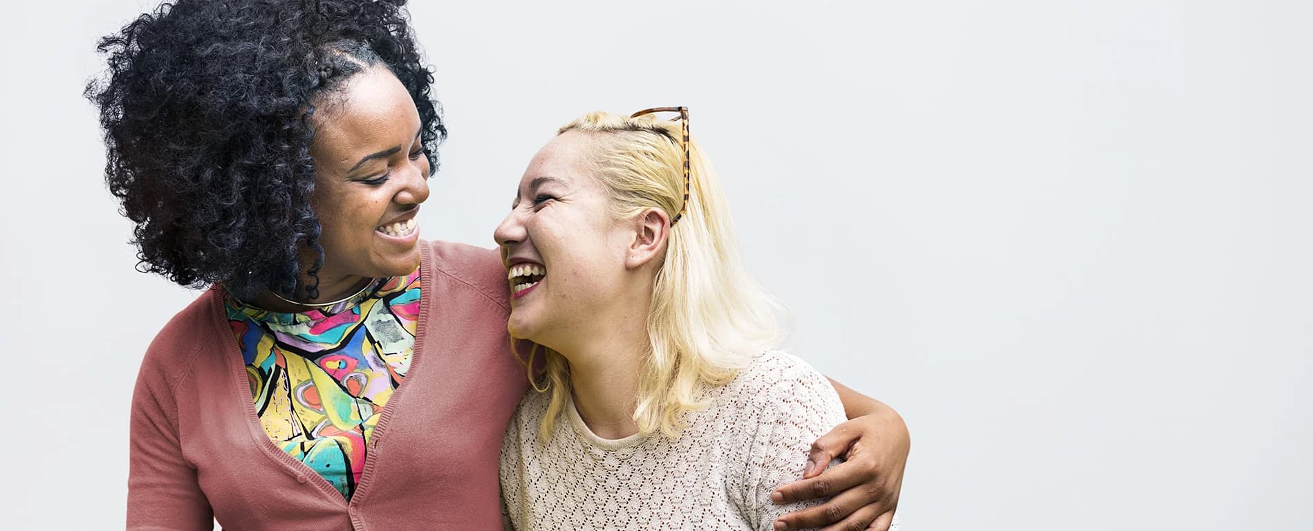 Two women smiling and laughing together, with one putting an arm around the other.