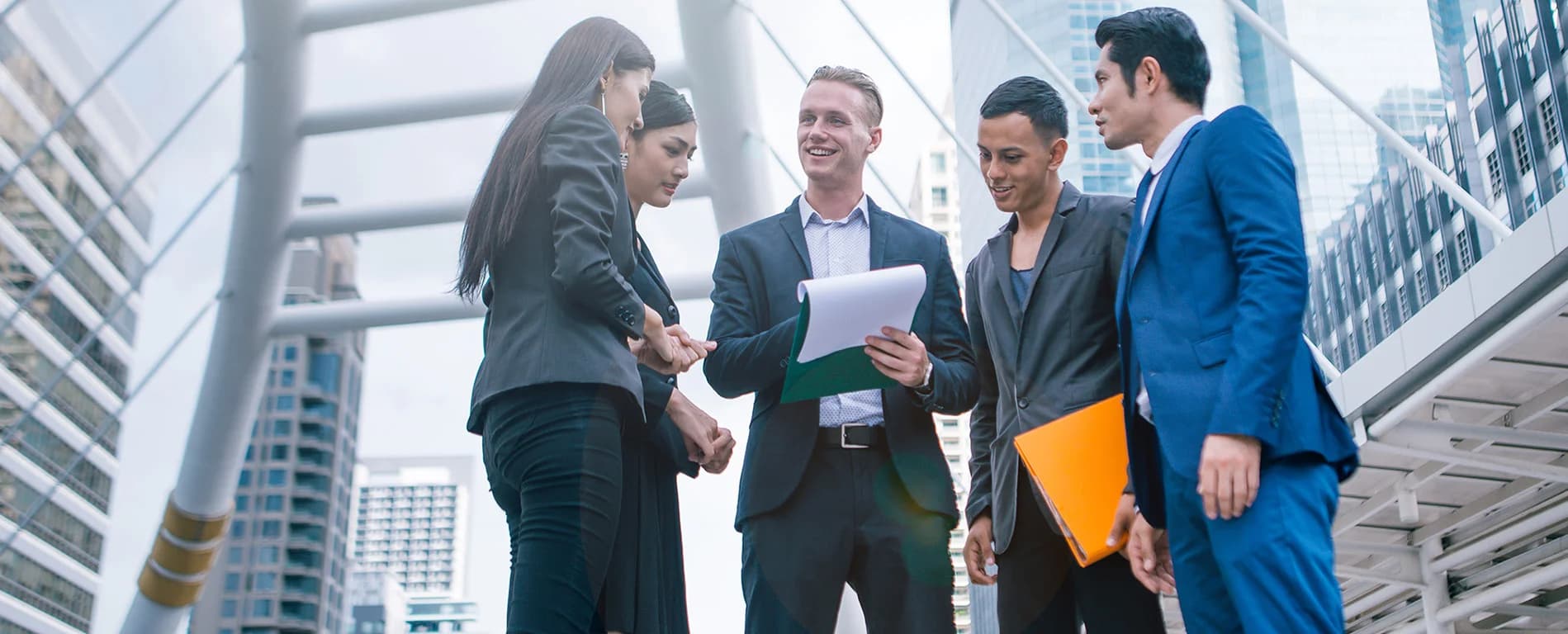 Group of business professionals meeting outdoors, discussing documents and shaking hands.